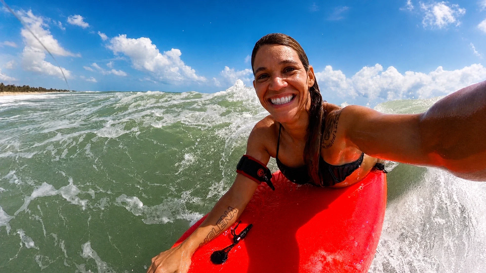 Isabela Sousa sorrindo no mar com uma prancha de bodyboard vermelha