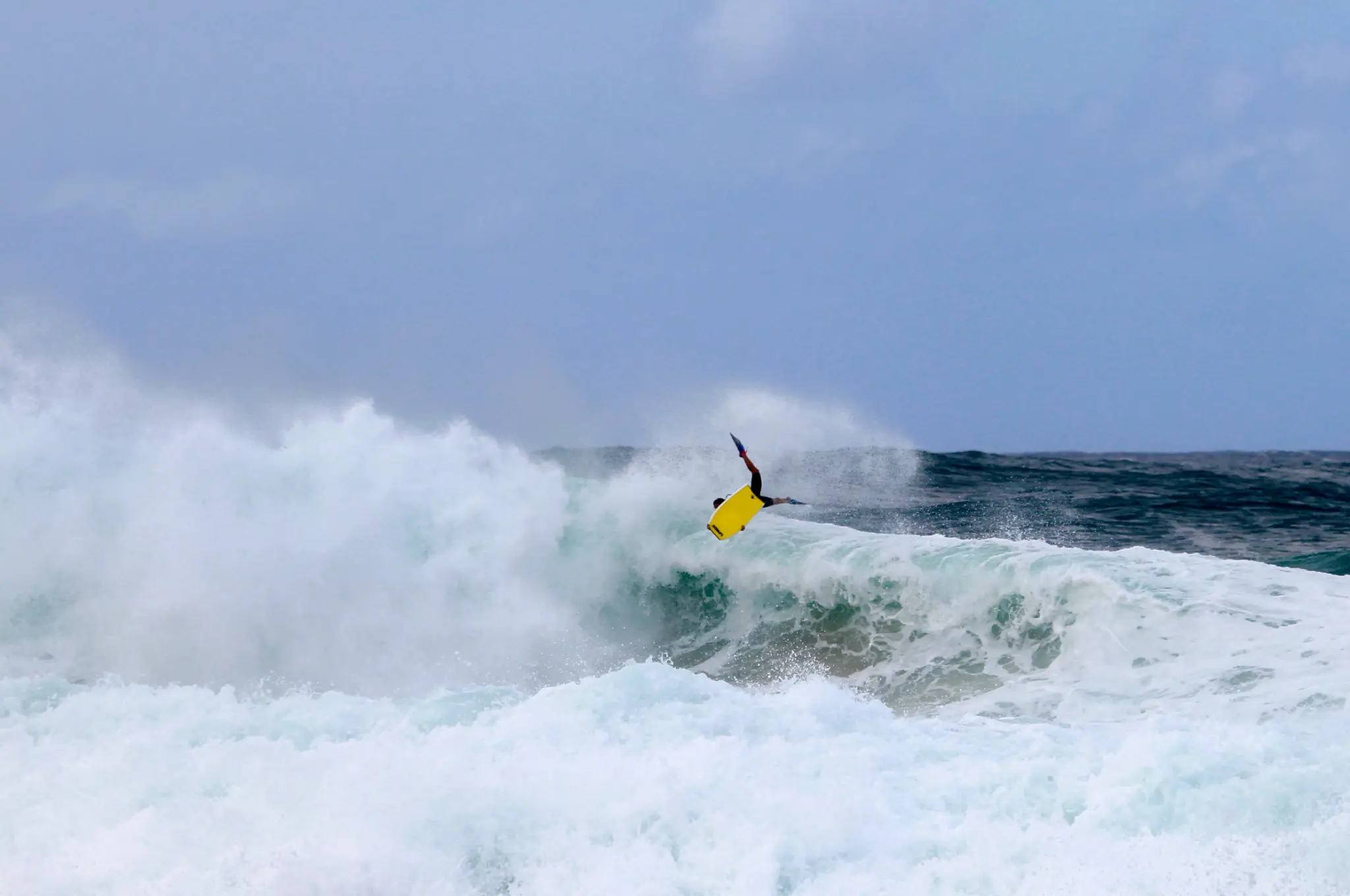 Isabela em manobra de bodyboard com prancha amarela sobre uma onda